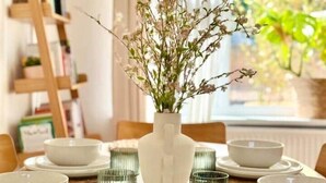 A dining table set with white plates, bowls, and green glassware, centered with a white vase containing branches and flowers. - The View on Castle Hill with Jacuzzi (Conwy)