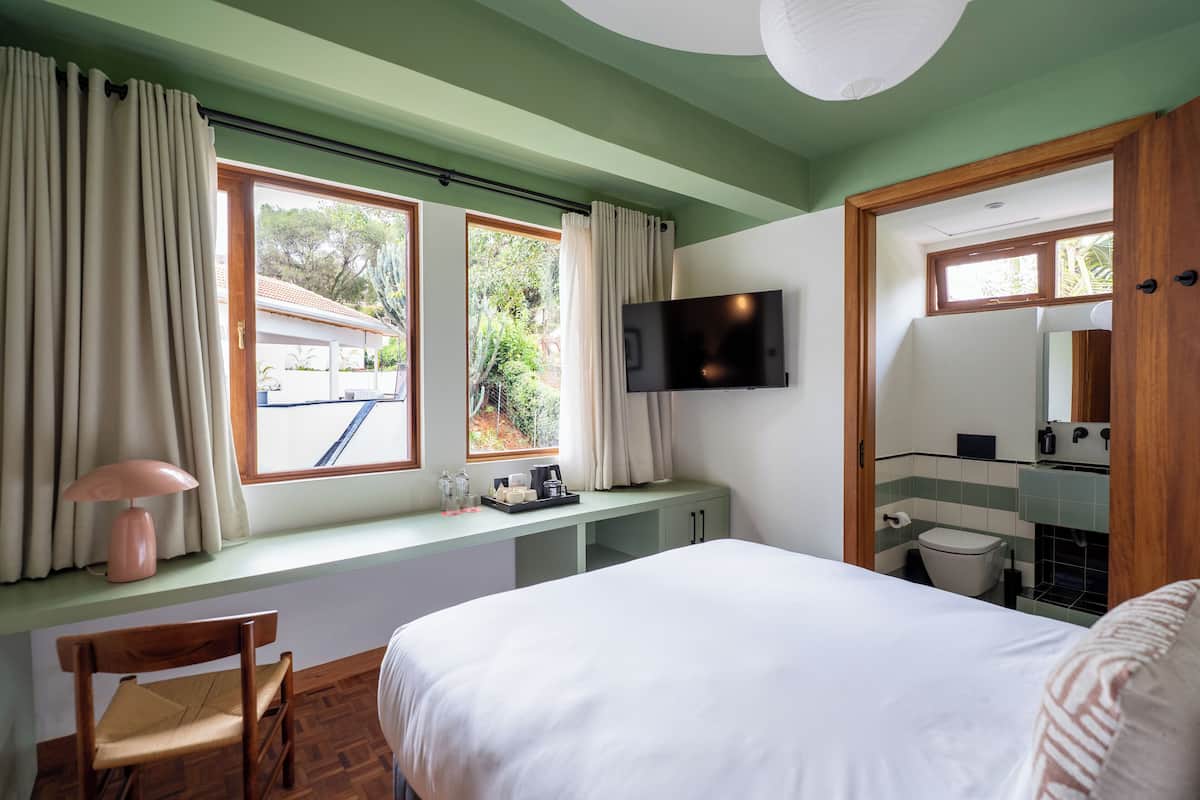 Une chambre à coucher avec un lit, un bureau, une chaise, une télévision et une salle de bain visible à travers une porte ouverte.
