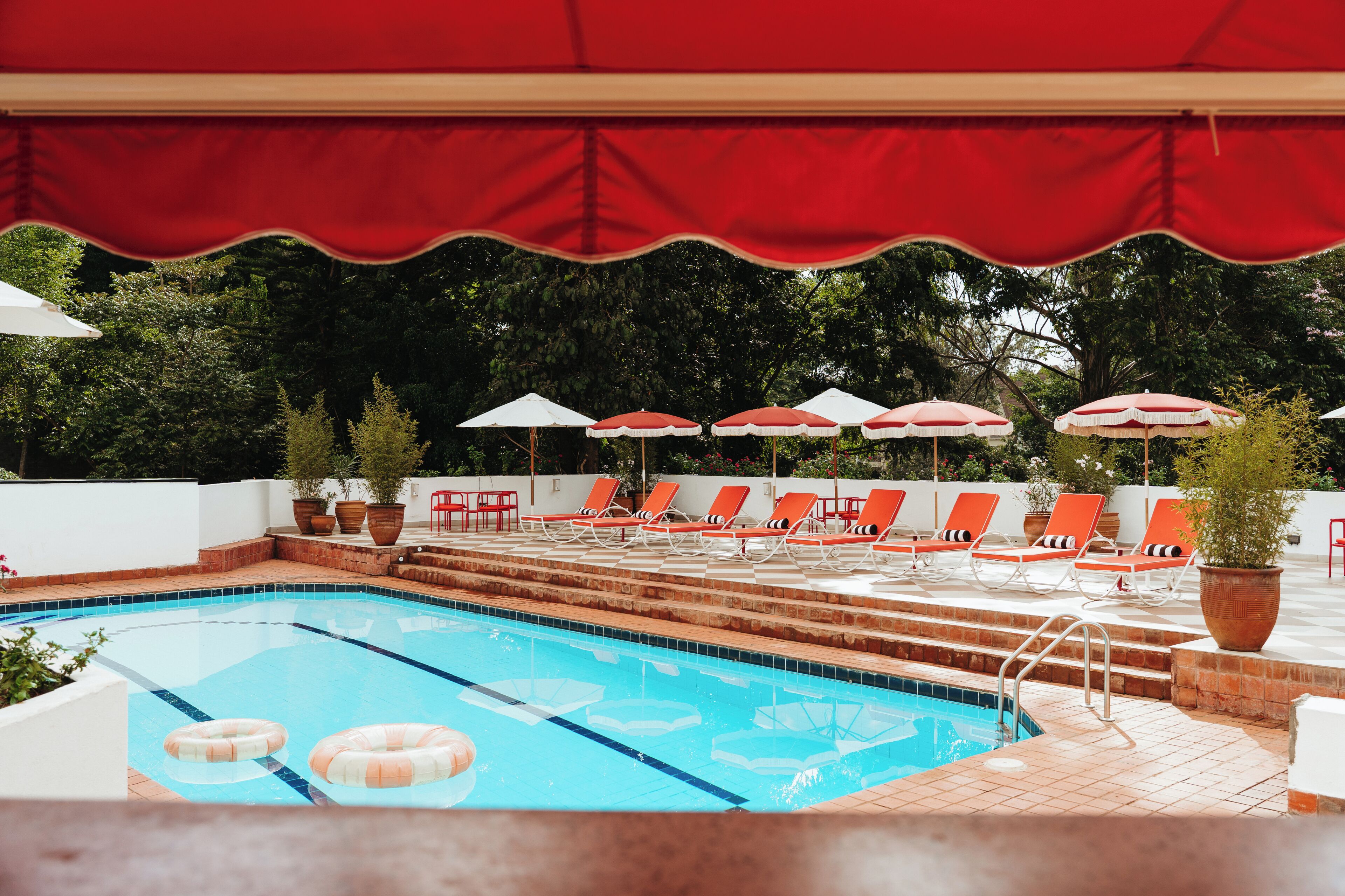 A swimming pool with lounge chairs and umbrellas, surrounded by potted plants and steps leading into the water.