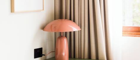 Een lamp op een groene plank, een lijst met een foto aan de muur, en een raam met gordijnen.