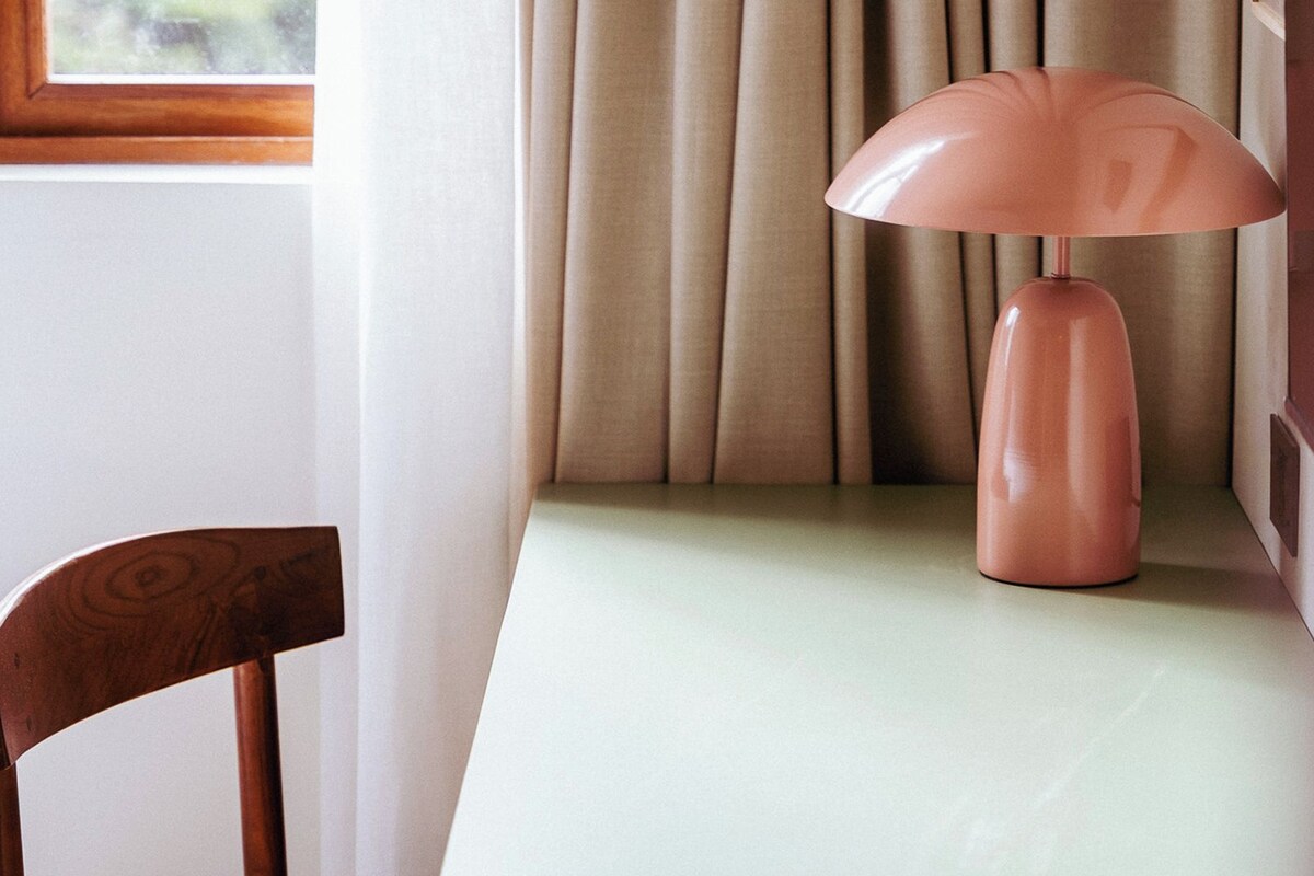 A room with a wooden chair, a table, and a pink lamp.