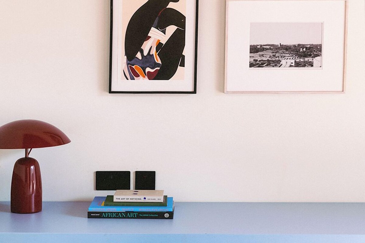 Ein Schreibtisch mit einer roten Lampe, zwei gerahmten Kunstwerken und einem Stapel Bücher.
