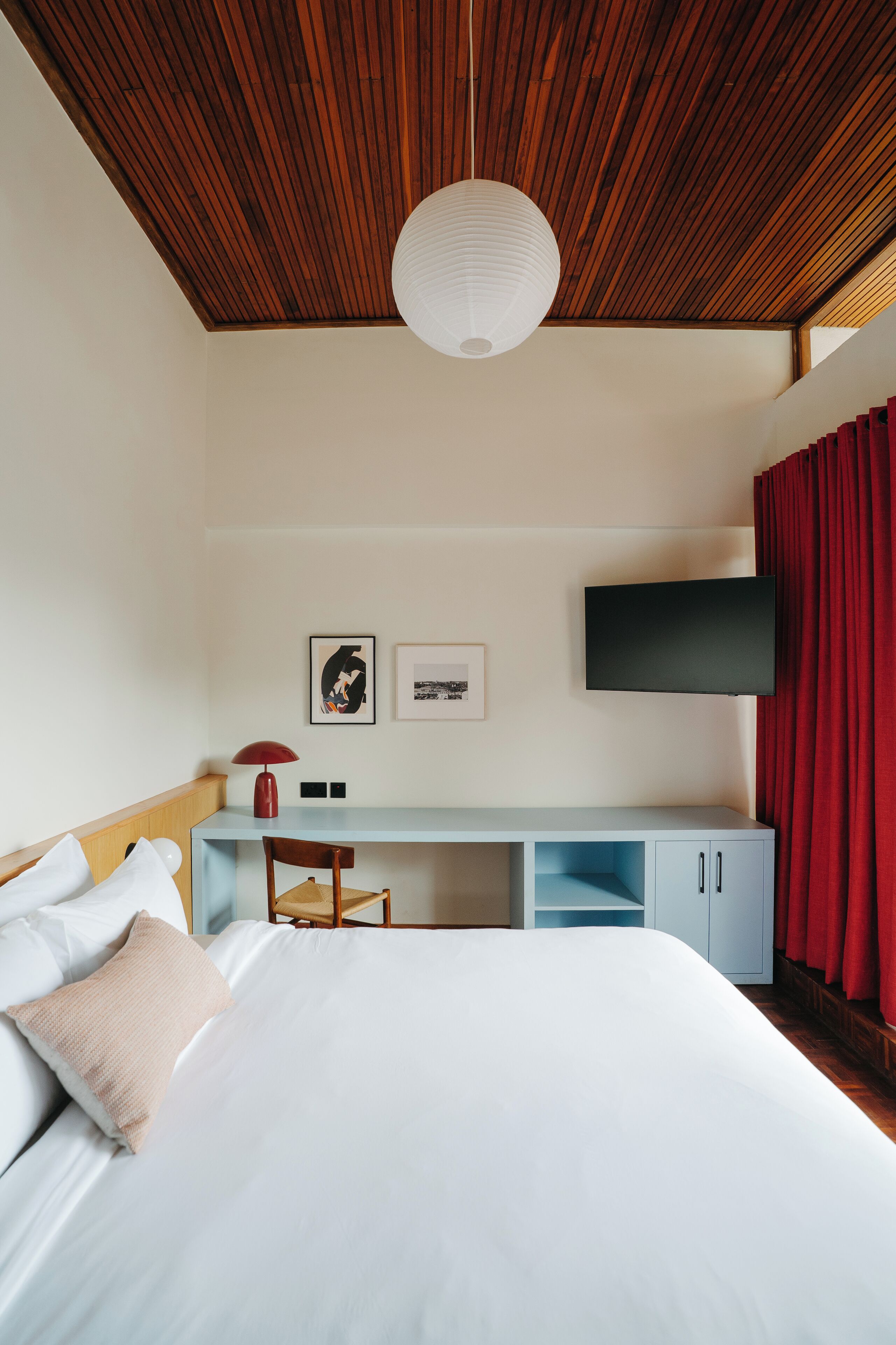A hotel room with a bed, a desk, a chair, a TV, and red curtains.