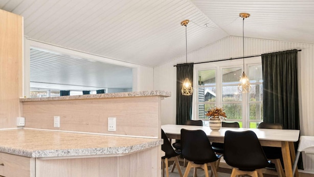 A modern kitchen with a granite countertop, wooden cabinets, and a dining area with a table and chairs. - 5 Star Holiday Home in Slagelse (Slagelse)