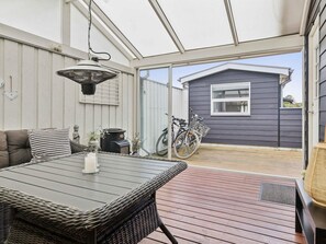 Eine überdachte Terrasse mit Tisch und Stühlen, ein Fahrrad und ein kleines Gartenhaus im Hintergrund.