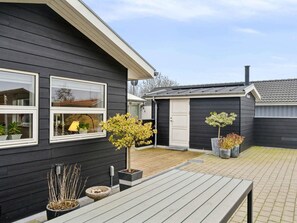 Ein schwarzes Haus mit weißen Verzierungen, einer Holzterrasse und einem kleinen Schuppen.