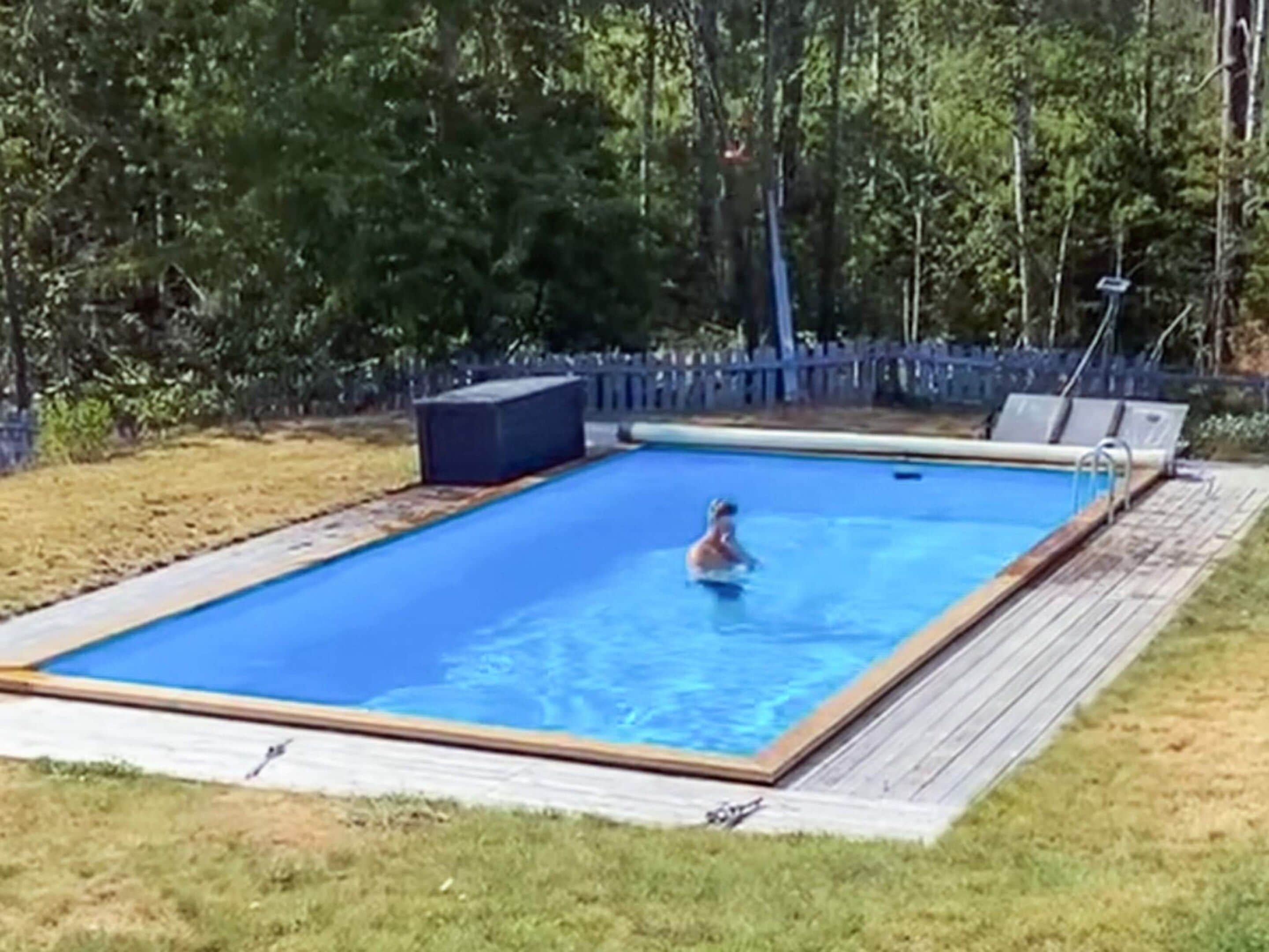A rectangular swimming pool with a wooden deck surrounding it.
