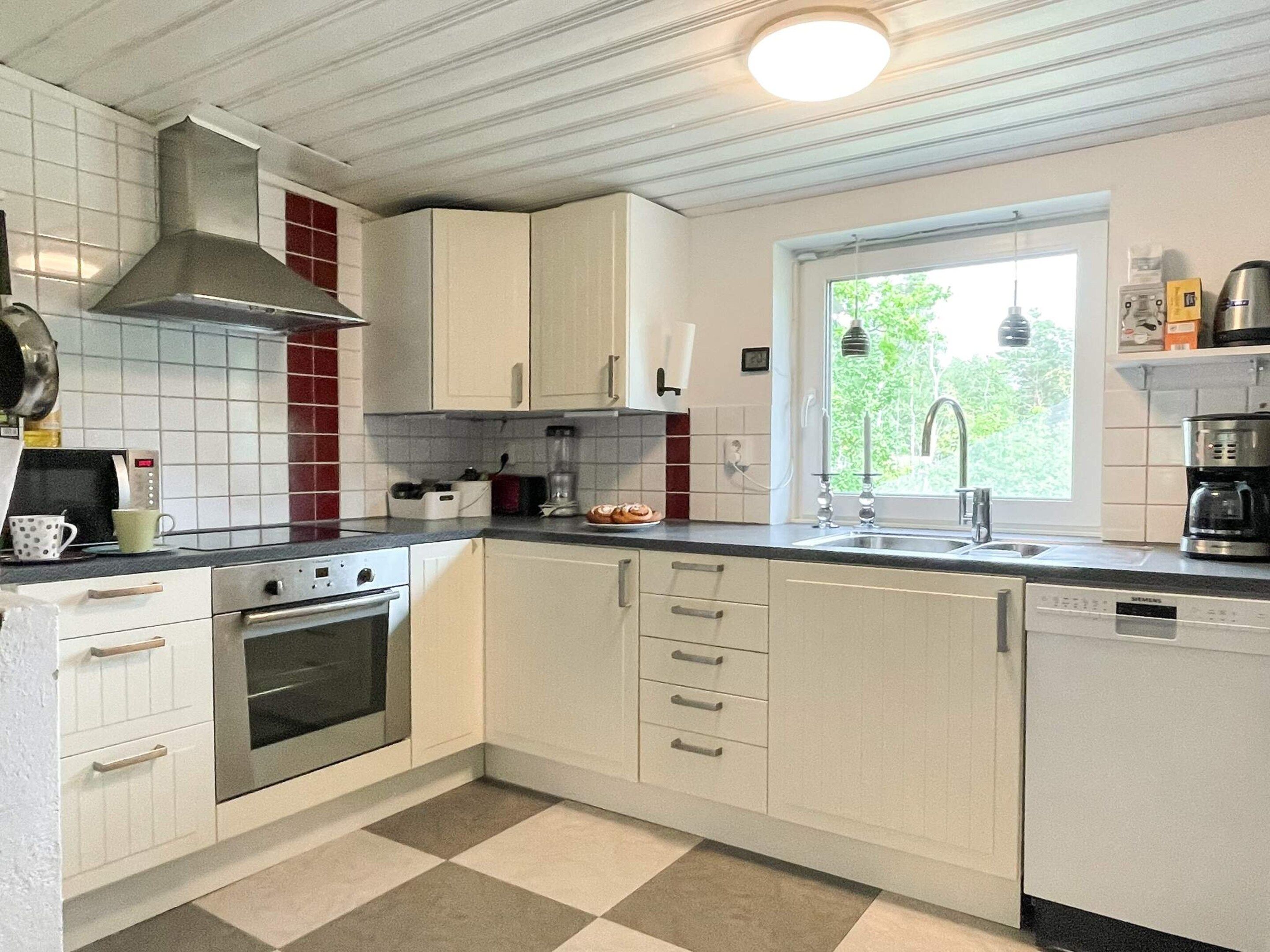 Une cuisine avec des meubles blancs, une cuisinière, un four et une fenêtre donnant sur un paysage verdoyant.