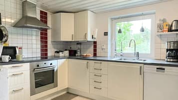 A kitchen with white cabinets, a stove, oven, and a window with a view of greenery.