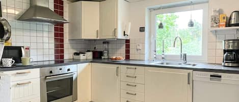 A kitchen with white cabinets, a stove, oven, and a window with a view of greenery.