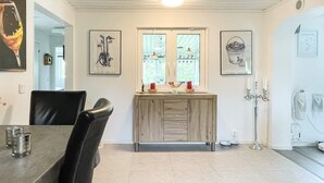 Ein Essbereich mit Holztisch und Stühlen, einem hellen Fliesenboden und Kunstwerken an den Wänden.