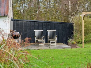 A patio area with two Adirondack chairs, a barbecue grill, and a wooden pergola. - 5 Star Holiday Home in Thyholm (Thyholm)