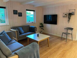 Un salon confortable avec un canapé, une table basse, un téléviseur et un fauteuil.