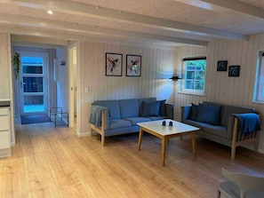 Un salon avec un plancher en bois, deux canapĂ©s, une table basse et des Ćuvres dâart encadrĂ©es accrochĂ©es au mur.