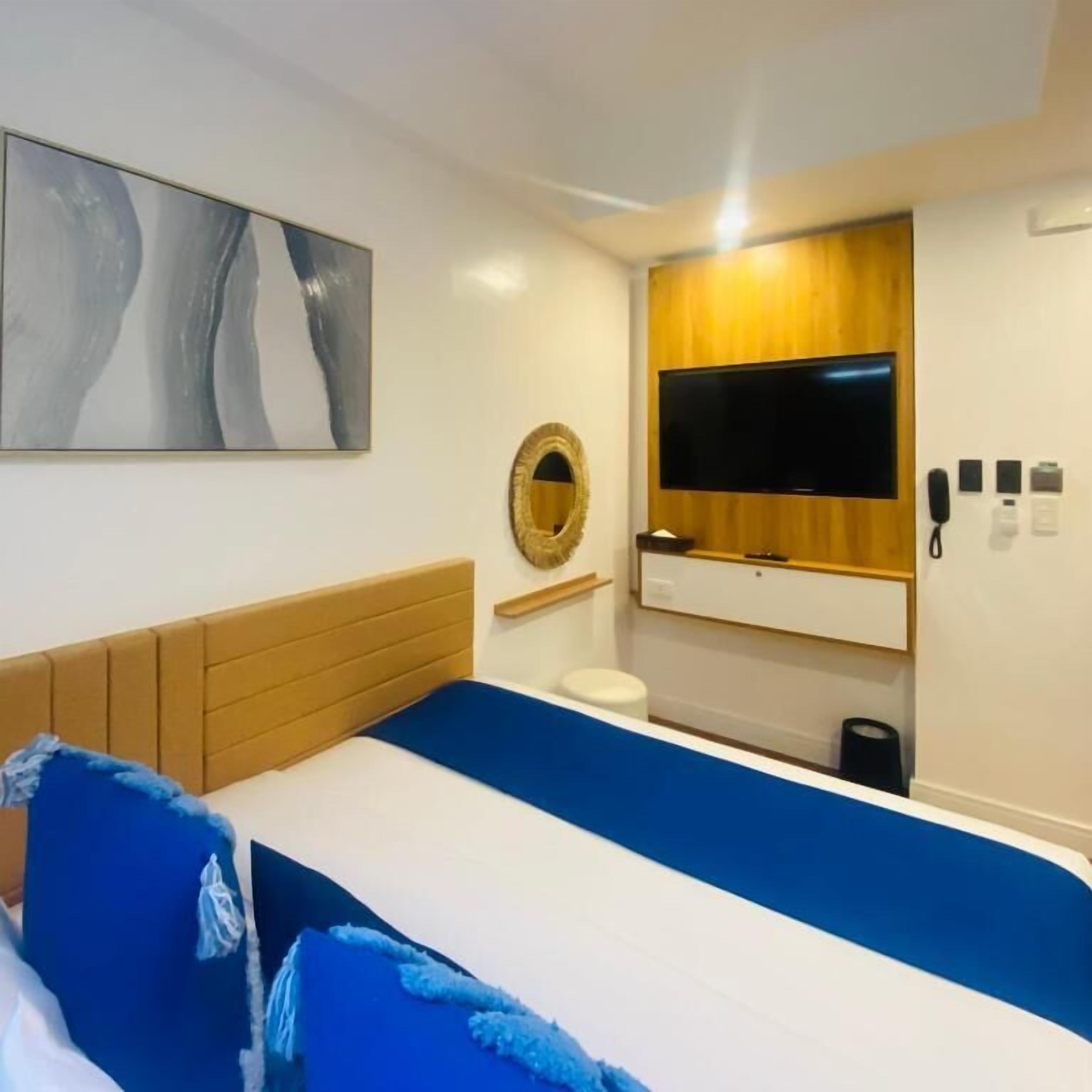 A hotel room with a bed, a mounted TV, a wooden panel wall, and a painting.