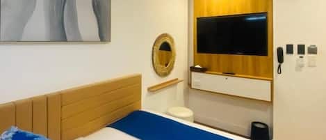 A hotel room with a bed, a mounted TV, a wooden panel wall, and a painting.