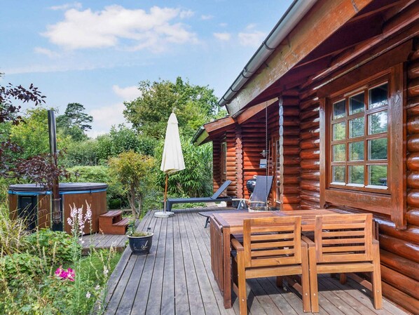 Une cabane en bois avec une terrasse, un barbecue et un fauteuil de relaxation.