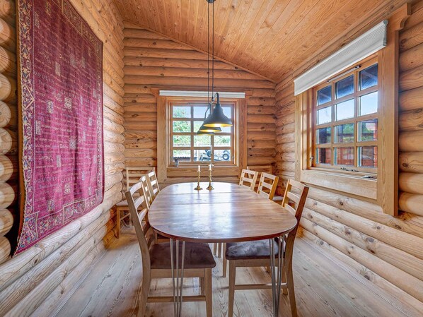 Una sala da pranzo in legno tipica di una baita, con un tavolo e sedie di legno, un lampadario e un'ampia finestra con persiane multiple.