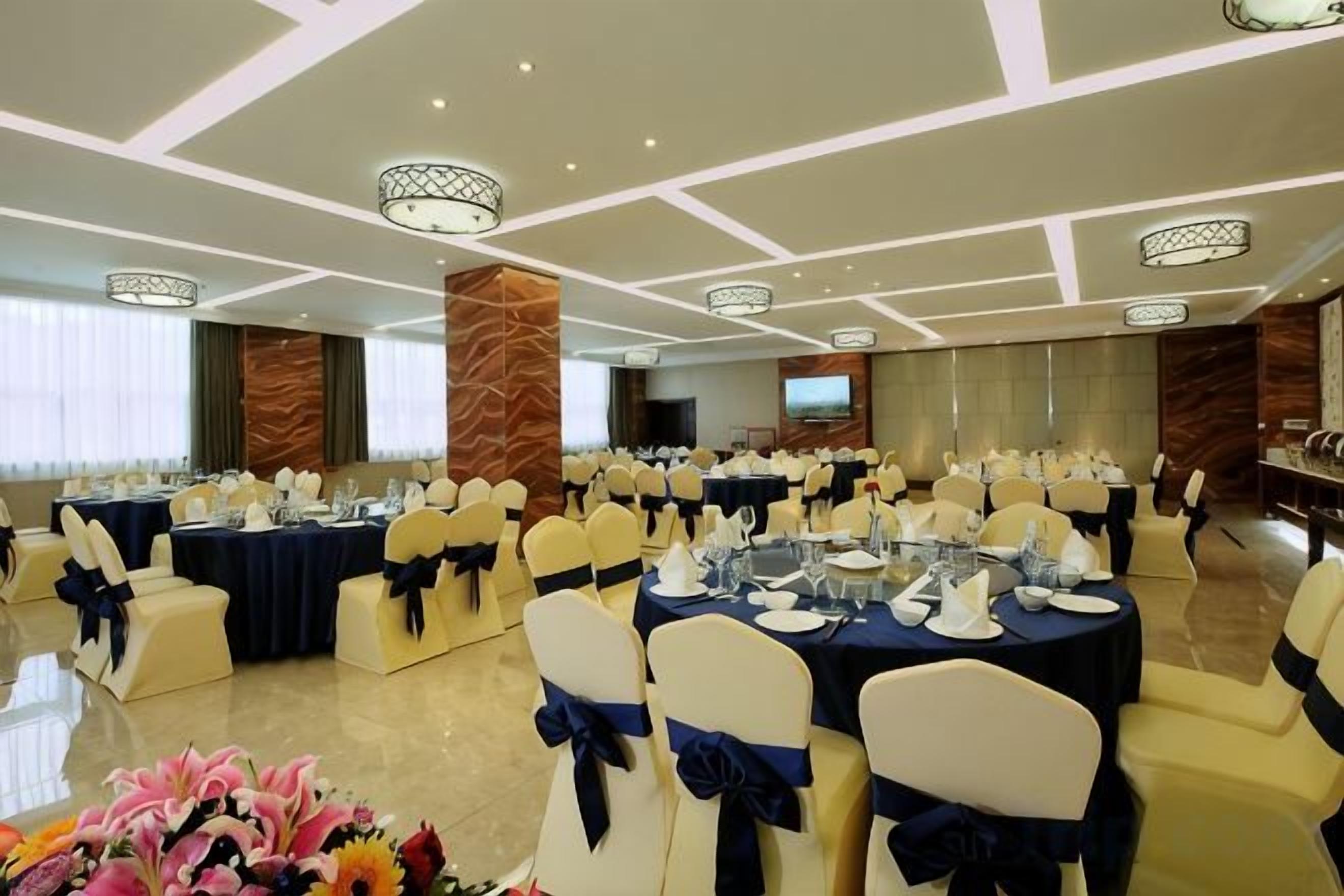 A banquet hall with round tables, chairs, and a television screen.