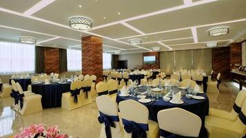 A banquet hall with round tables, chairs, and a television screen.