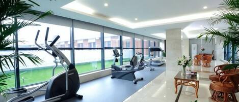 A modern gym with exercise equipment, large windows, and indoor plants.