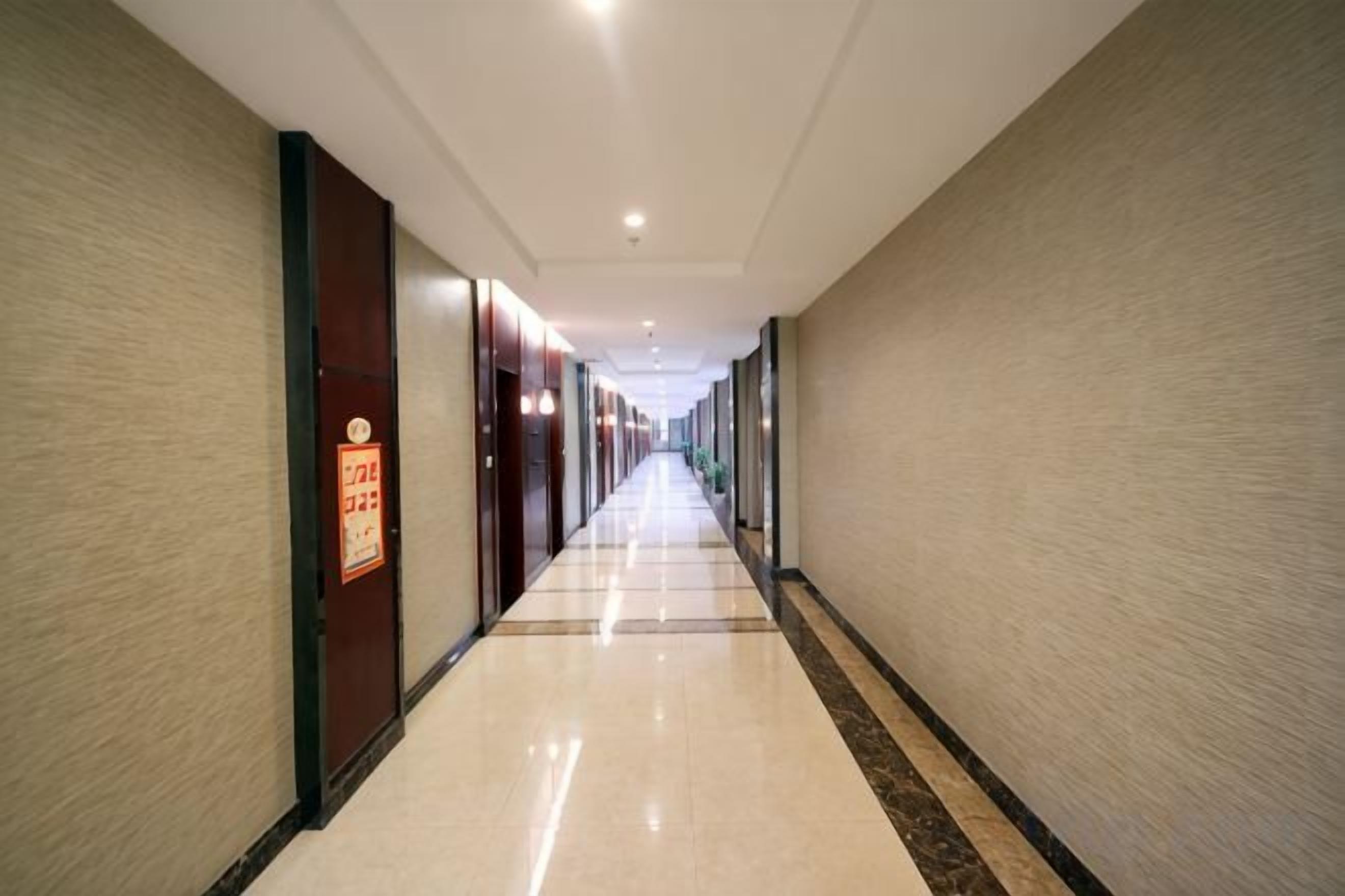 A long, narrow hotel corridor with doors on both sides, a tiled floor, and a ceiling with recessed lighting.