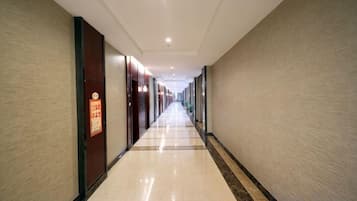 A long, narrow hotel corridor with doors on both sides, a tiled floor, and a ceiling with recessed lighting.