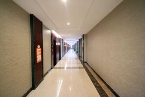 Een lange, smalle hotelgang met deuren aan beide kanten, een betegelde vloer en een plafond met inbouwverlichting.