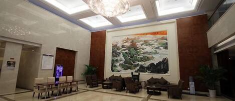 A lobby with a large painting, a chandelier, and seating arrangements.