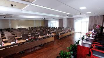A conference room with rows of tables and chairs, large windows, and a wooden floor.