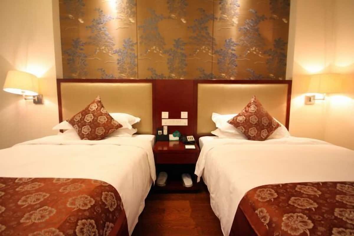 A hotel room with two beds, a nightstand with a phone and a lamp, and a wall with a floral pattern.