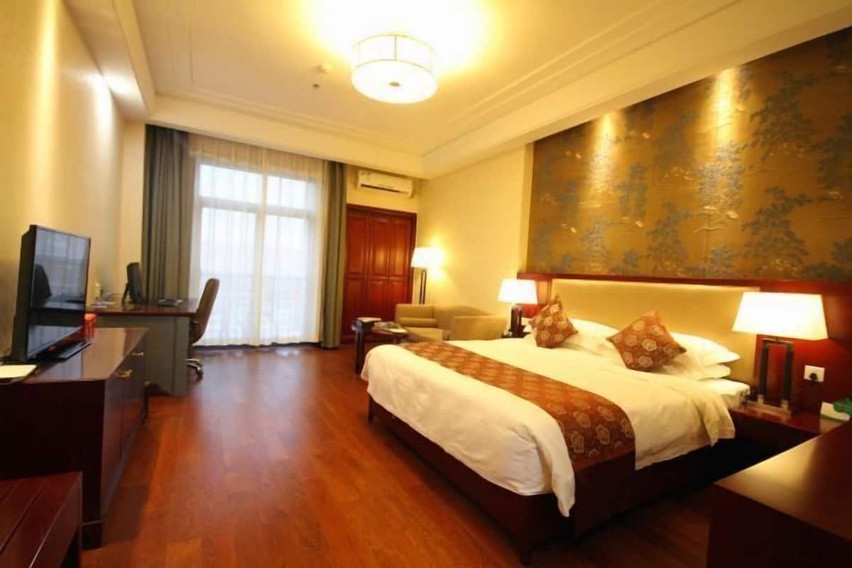 A hotel room with a large bed, desk, and chair, a television, and a large window with curtains.