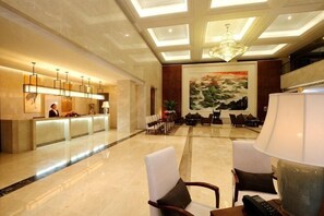 A hotel lobby with a reception desk, seating area, and a large painting on the wall.