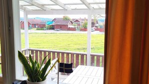 Eine überdachte Veranda mit Blick auf ein grünes Feld und Häuser im Hintergrund.