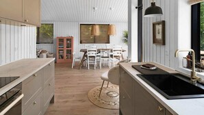A modern kitchen with white wooden walls, a large window, and a dining area with a table and chairs. - 5 Star Holiday Home in Hasle (Nykobing Sjaelland)