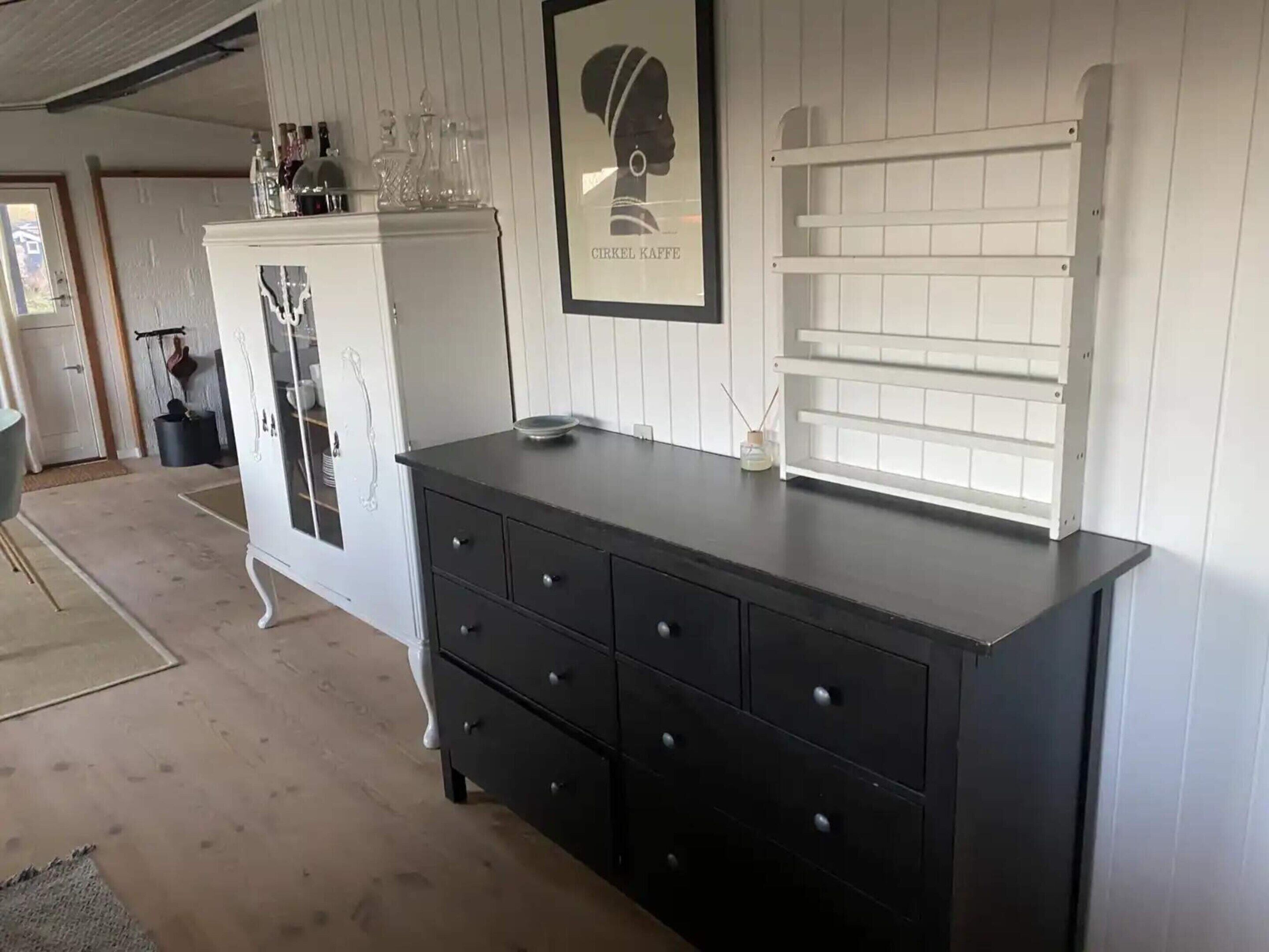 Una habitación con un aparador negro, un armario blanco y un cuadro en la pared.