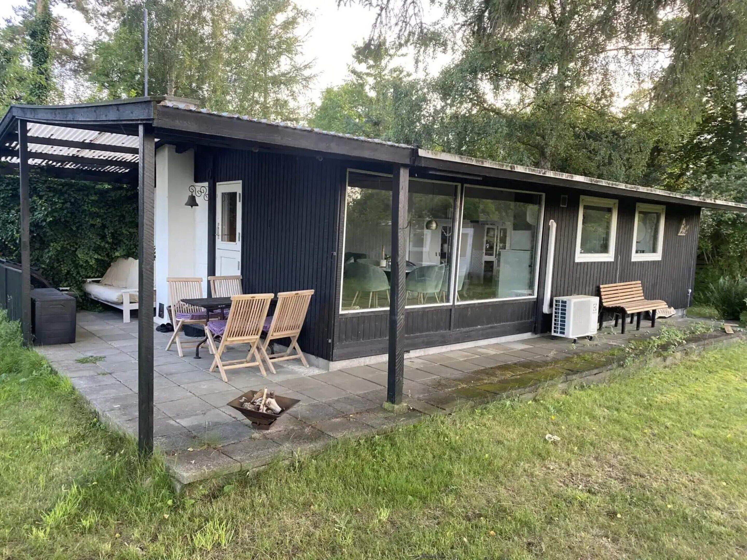 Una casa pequeña y moderna con un patio que cuenta con una mesa, sillas, una fogata y un banco.