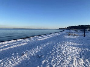 Een strand bedekt met sneeuw, met een heldere lucht en een rustige zee.