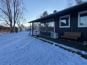 Een overdekte veranda met een bankje, een sneeuwbedekte tuin en een gebouw met grote ramen.