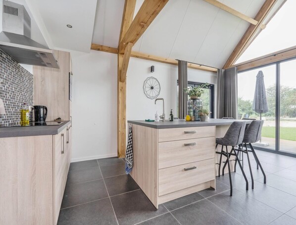A modern kitchen with a wooden island, a dining area with chairs, and a large window offering a view. - Modern Lodge Stay With Pond View (Baarle-Nassau)