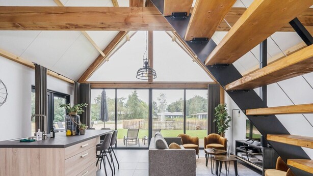 A modern kitchen with a large island, a dining area with a sofa and chairs, and a view of the outdoors through large windows. - Modern Lodge Stay With Pond View (Baarle-Nassau)
