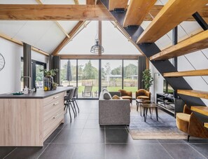 A modern kitchen with a large island, a dining area with a sofa and chairs, and a view of the outdoors through large windows. - Modern Lodge Stay With Pond View (Baarle-Nassau)