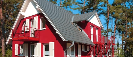 A red and white two-story house with a grey roof, surrounded by trees.