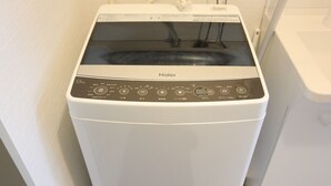 Une machine à laver Haier dans une pièce aux murs et à la porte blancs.