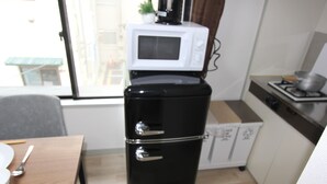 Une cuisine de taille réduite avec un réfrigérateur noir, un four à micro-ondes blanc placé sur le dessus, et une cuisinière.