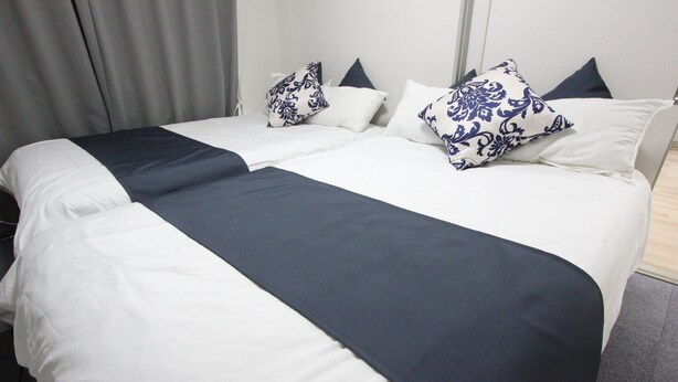 Un lit double avec une literie blanche et bleu foncé, deux coussins décoratifs et un rideau gris.