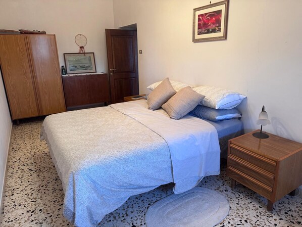 A bedroom with a bed, a wooden wardrobe, a nightstand, a lamp, and a framed picture on the wall.