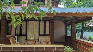 A covered outdoor seating area with a table and chairs, a brick wall, and a view of a building in the background.