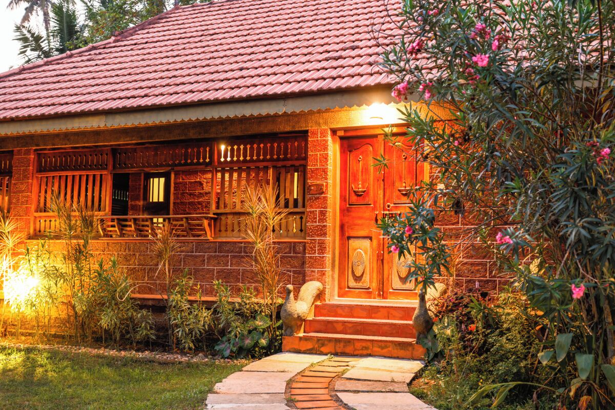 A traditional house with a red-tiled roof, a wooden front door, and a small garden with plants and a pathway leading to the entrance.