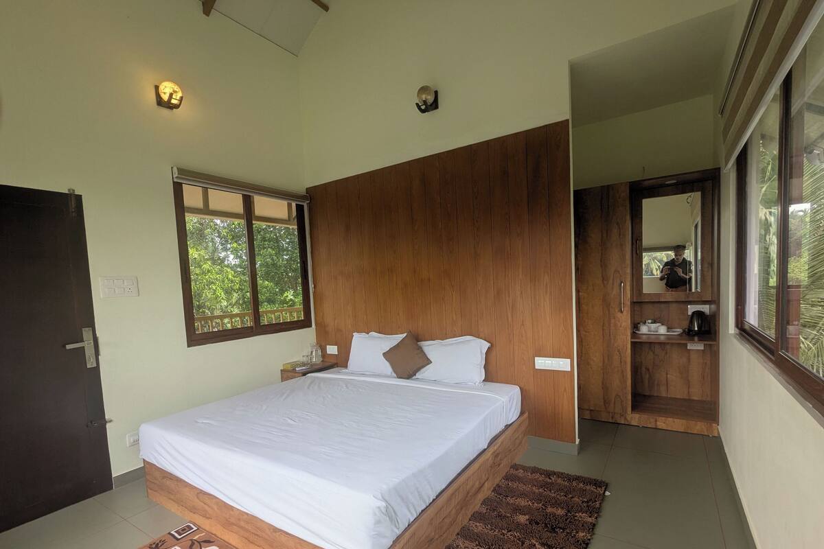 A bedroom with a wooden bed frame, a large window, a mirror, and a small bedside table.
